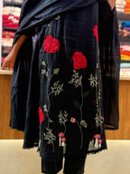 A black cotton kurta with red floral and green vine embroidery, paired with a matching black dupatta, shown on a model in a retail store.